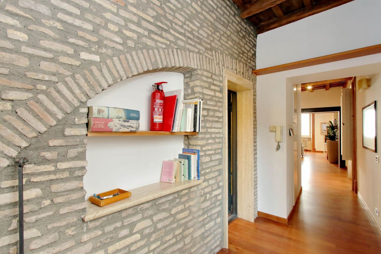 A room with a brick wall, wooden floor, and a bookshelf with books and a fire extinguisher.