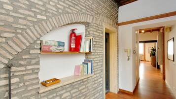 A room with a brick wall, wooden floor, and a bookshelf with books and a fire extinguisher.