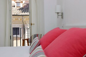 Ein Schlafzimmer mit Bett, Blick auf einen Innenhof und einer Wandlampe.