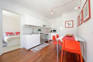 Cocina compacta con armarios blancos, lavavajillas y comedor con mesa y sillas rojas.