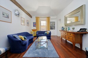 A living room with two blue sofas, a glass coffee table, a wooden dresser, and a large mirror.