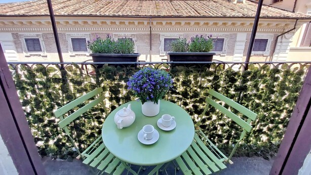 A balcony with a round table set for tea, surrounded by green chairs, and potted plants. - Superb Penthouse near Piazza Navona (Roma)