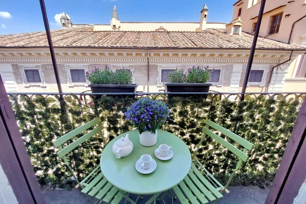 A balcony with a round table set for tea, surrounded by green chairs, and potted plants. - Superb Penthouse near Piazza Navona (Roma)