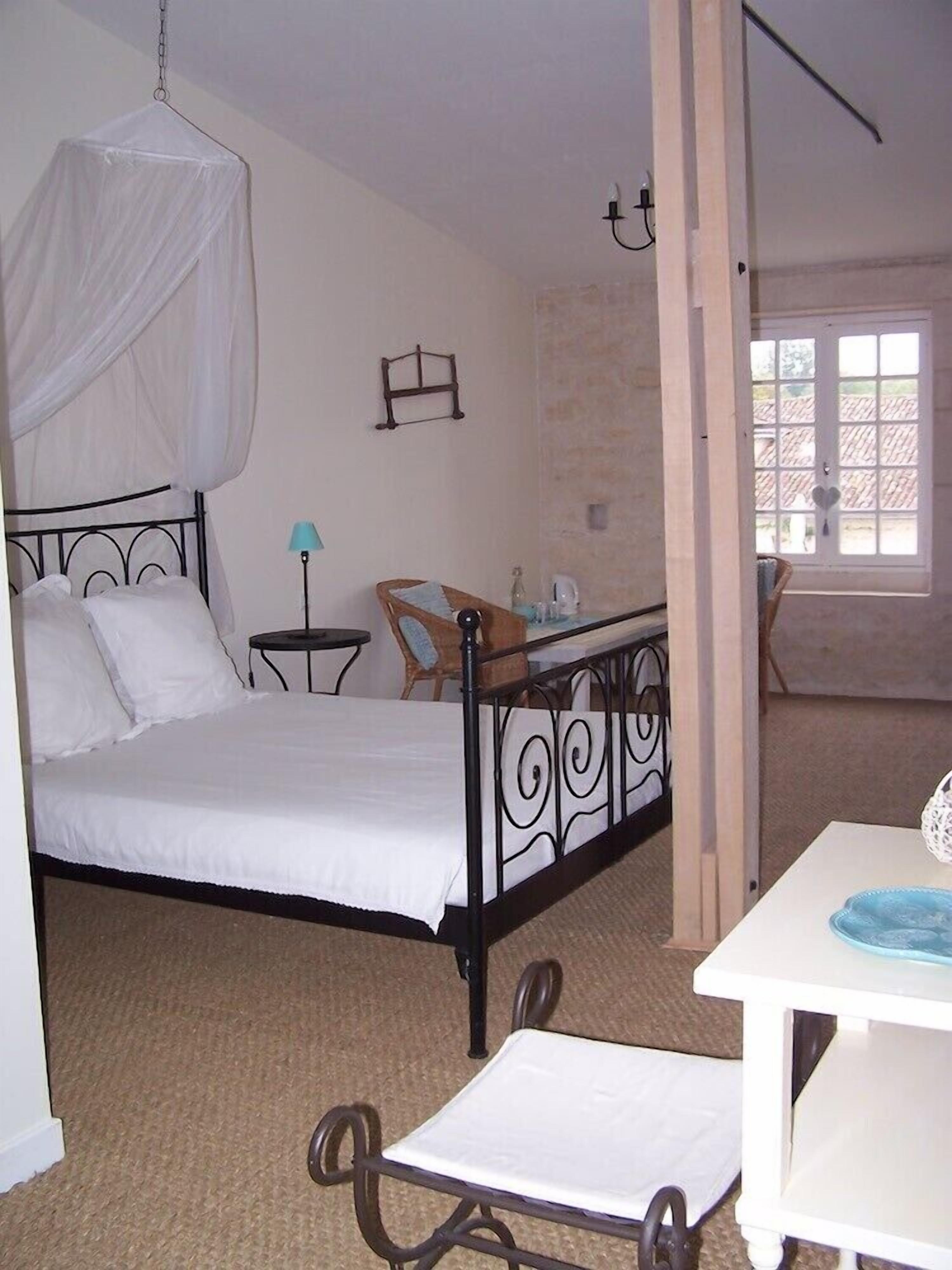 A bedroom with a bed, a chair, a table, and a window.