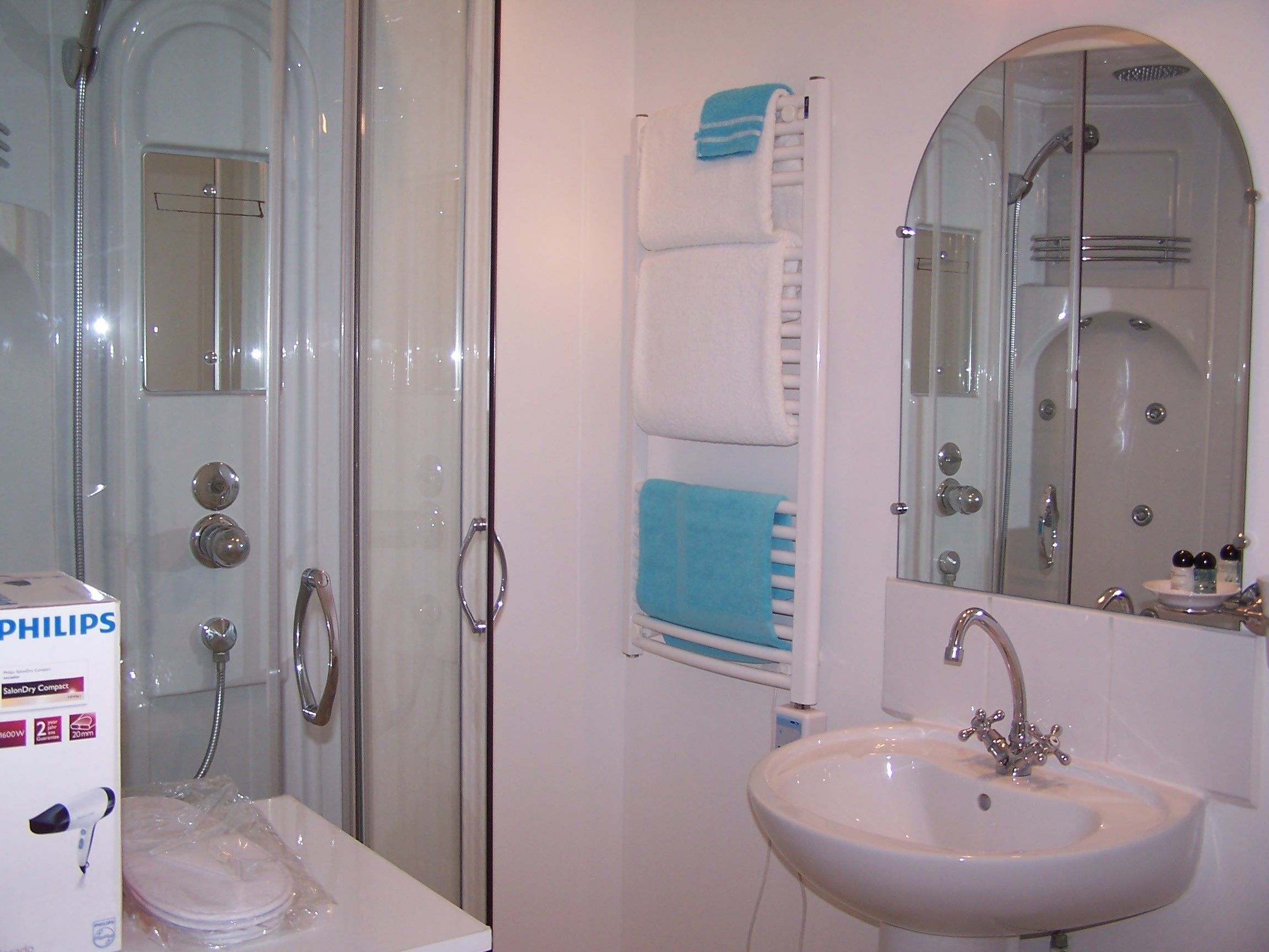 Une salle de bain avec une douche à parois de verre, un lavabo blanc et un porte-serviettes avec des serviettes bleues.