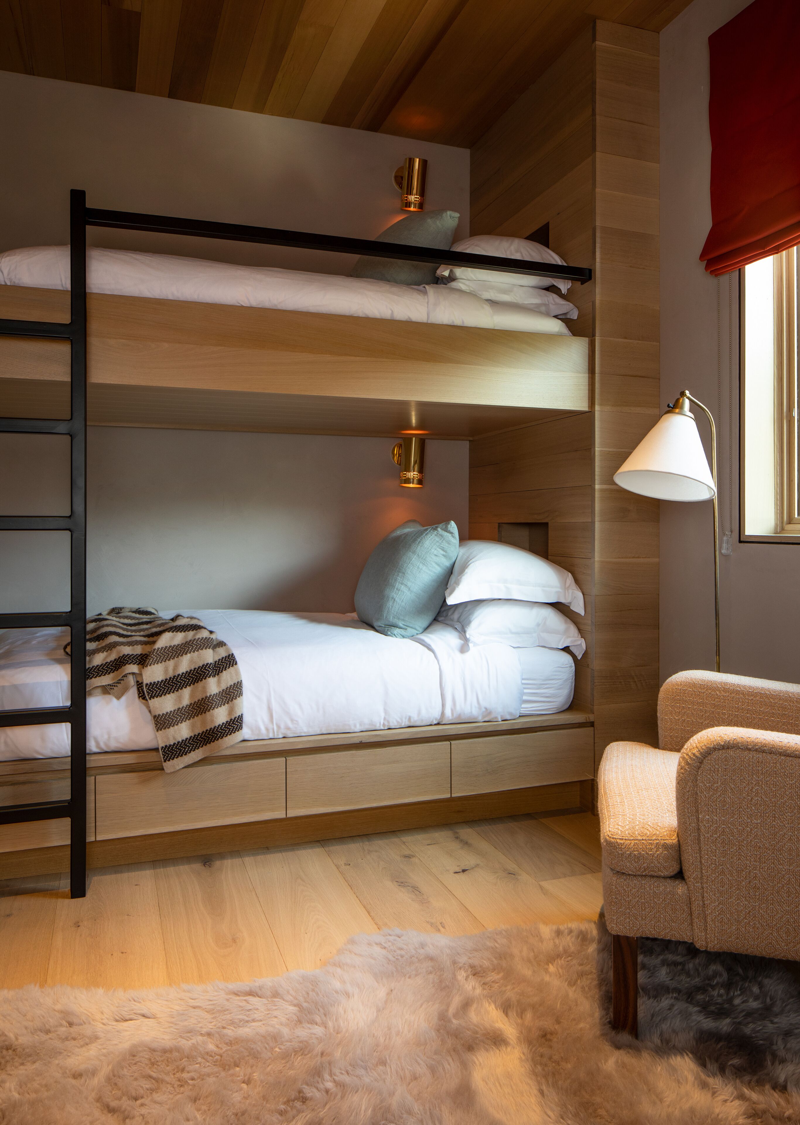 A bunk bed with a ladder, a bedside lamp, a chair, and a fur rug.