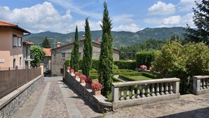 A stone pathway leading to a stone building with a red roof, surrounded by neatly trimmed hedges and tall cypress trees. - Villa La Fonte for 12 (San Godenzo)