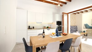 A modern kitchen with white cabinets, a wooden dining table, and a built-in oven. - Pius Eleven by Balearic Villas (Pollensa)