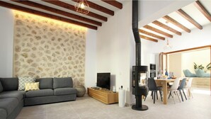 A modern living room with a sectional sofa, a TV, a fireplace, and a dining area with chairs and a table. - Pius Eleven by Balearic Villas (Pollensa)