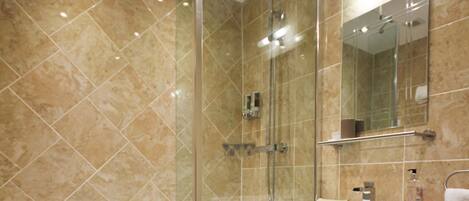 A modern bathroom with a glass-enclosed shower, a white sink, and a marble-tiled wall.