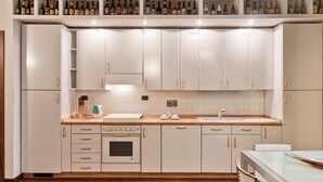 Une cuisine moderne avec des armoires blanches, un four encastré, un plan de travail avec une bouilloire et un porte-bouteilles de vin placé au-dessus des armoires.