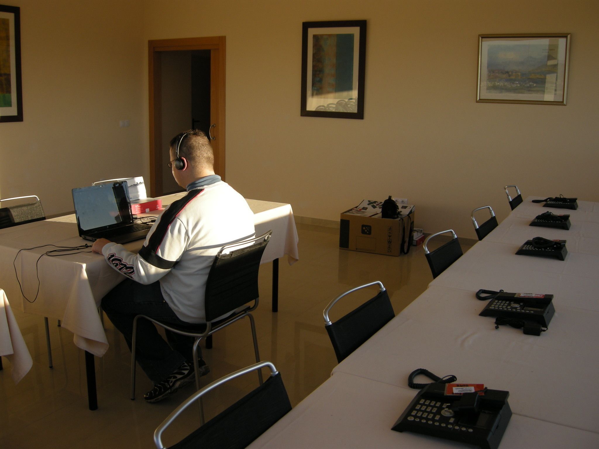 A conference room with a long table, chairs, and a person using a laptop.