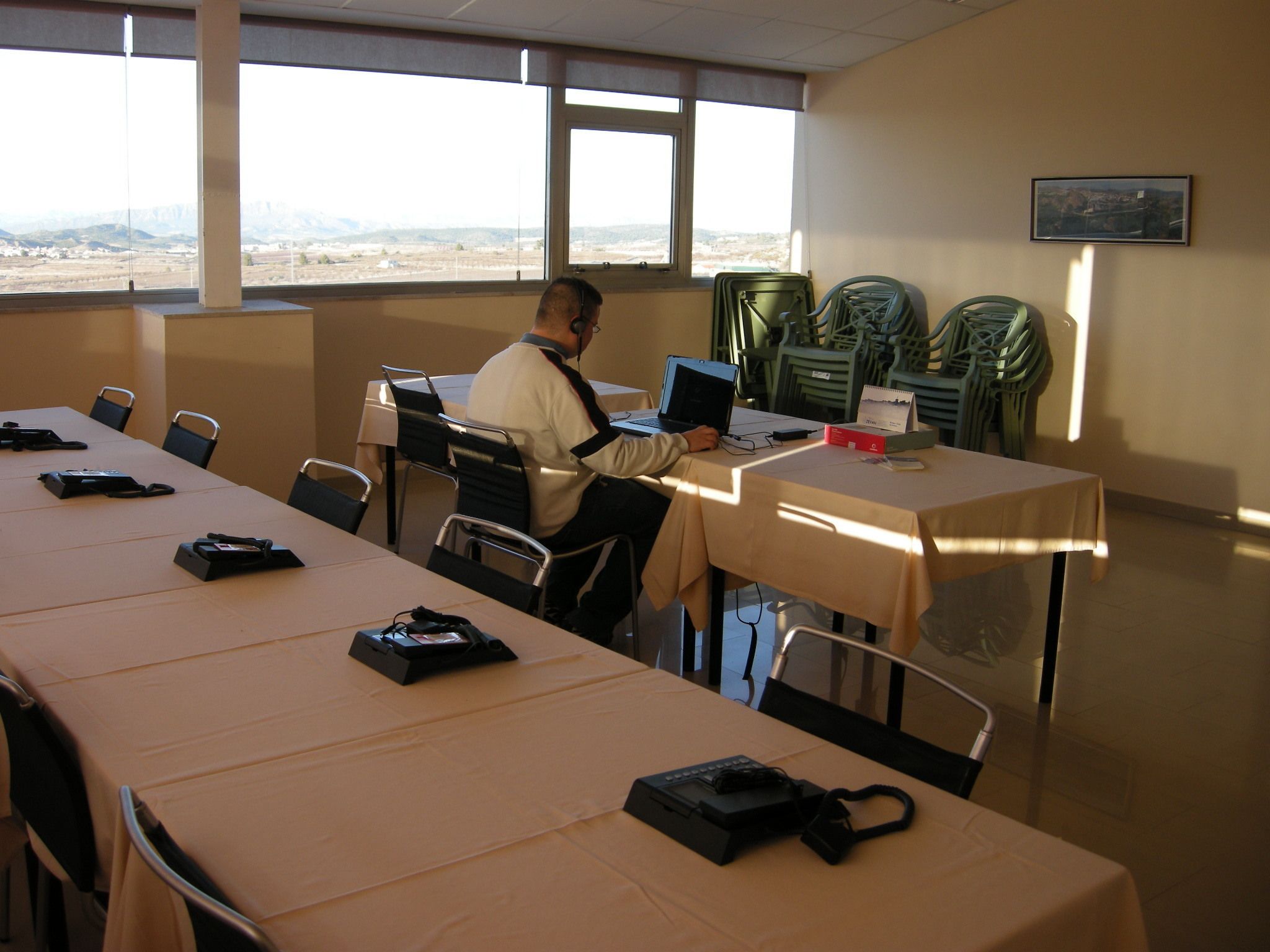 Een vergaderruimte met een lange tafel, stoelen en een persoon die een laptop gebruikt.