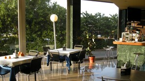 A restaurant with tables and chairs, a bar area, and a view of trees through large windows. - Hotel SG Bullas (Bullas)
