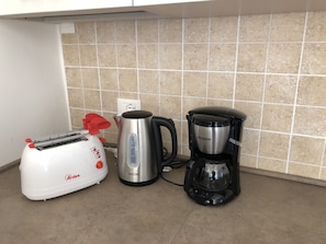 Cozinha com torradeira branca, chaleira elétrica de aço inoxidável e máquina de café preta no balcão.