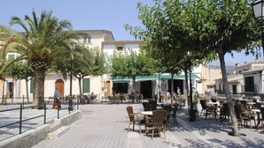 Un espace café en plein air, avec des tables et des chaises, entouré d’arbres et d’immeubles.