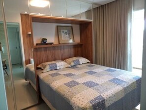 Een slaapkamer met een bed, een houten hoofdeinde, een lijst met een afbeelding en een raam met gordijnen.