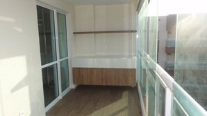 Un balcón con piso de madera, puertas de vidrio y una pared blanca con estante de madera.