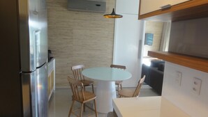 Una cocina compacta con una mesa redonda, sillas de madera, un refrigerador y una lámpara colgante.