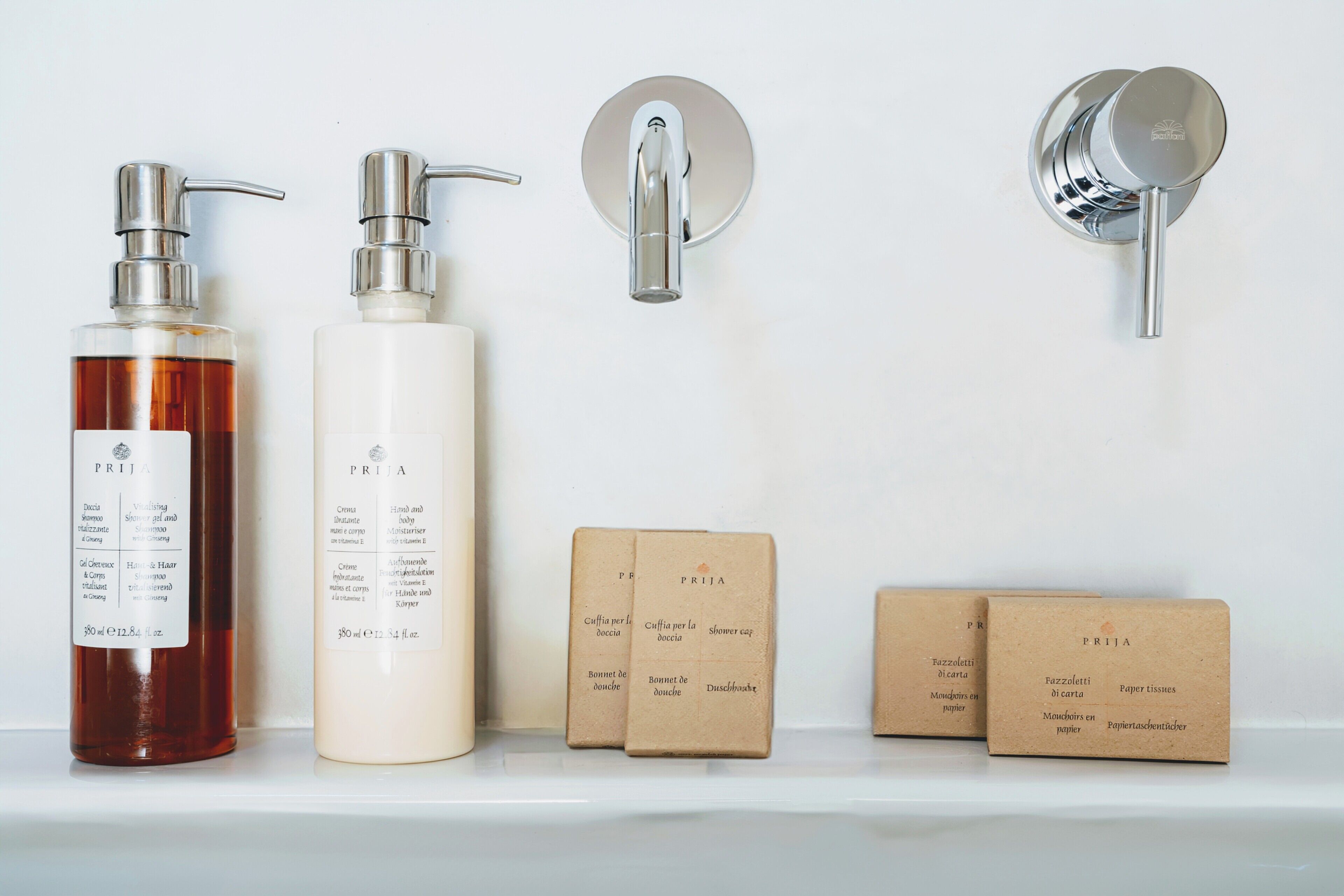 Uma prateleira no banheiro com duas garrafas de shampoo, um dosador de sabonete e duas pequenas caixas de papel toalha.
