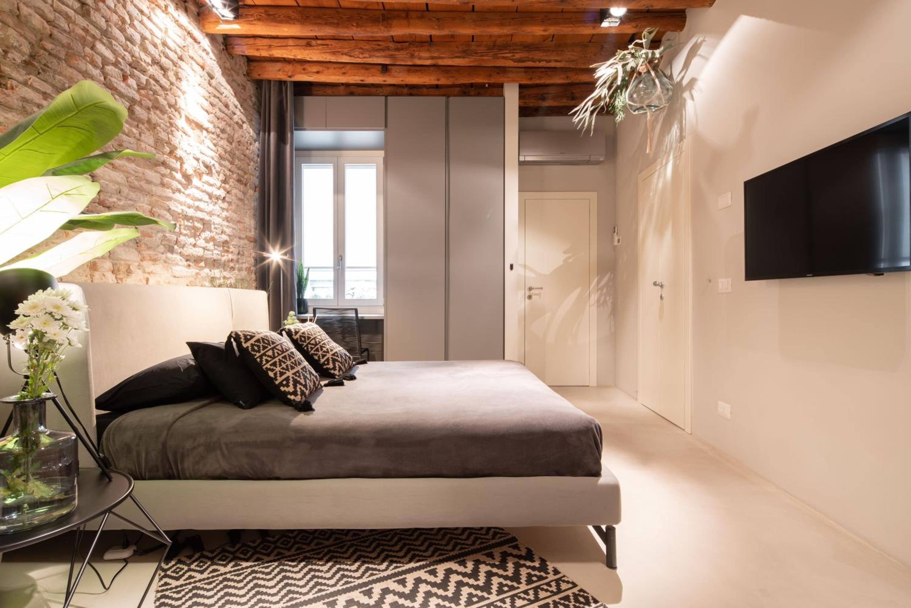 Une chambre avec un lit, une télévision, une plante et un mur en briques.
