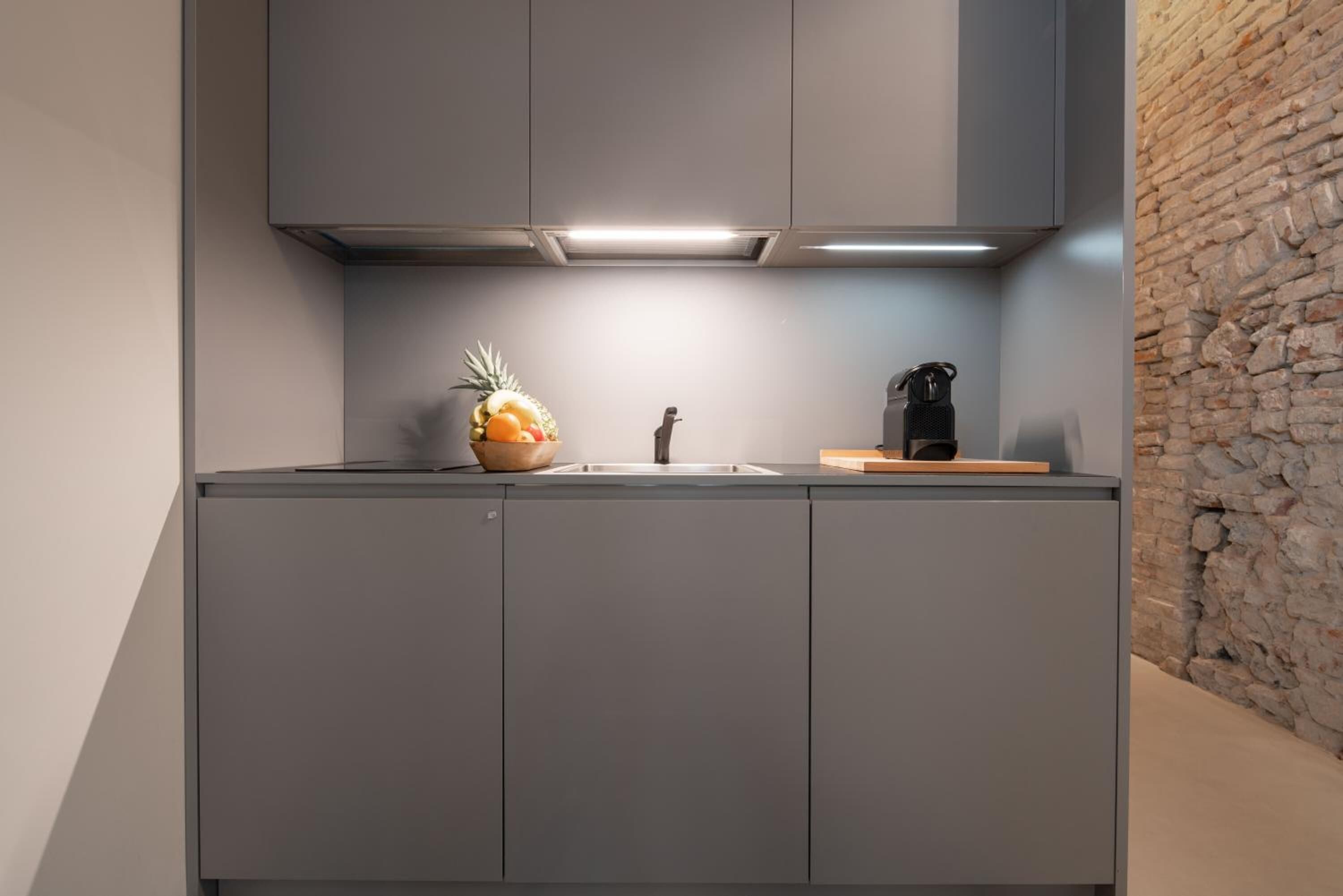Eine moderne Küche mit grauen Schränken, einer Edelstahlspüle, einer Obstschale und einer Kaffeemaschine.