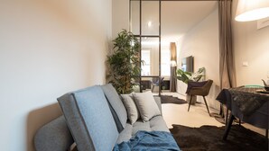 A modern living room with a sofa, a dining table, and a large plant. - Officine Cavour Apartments (Padova)