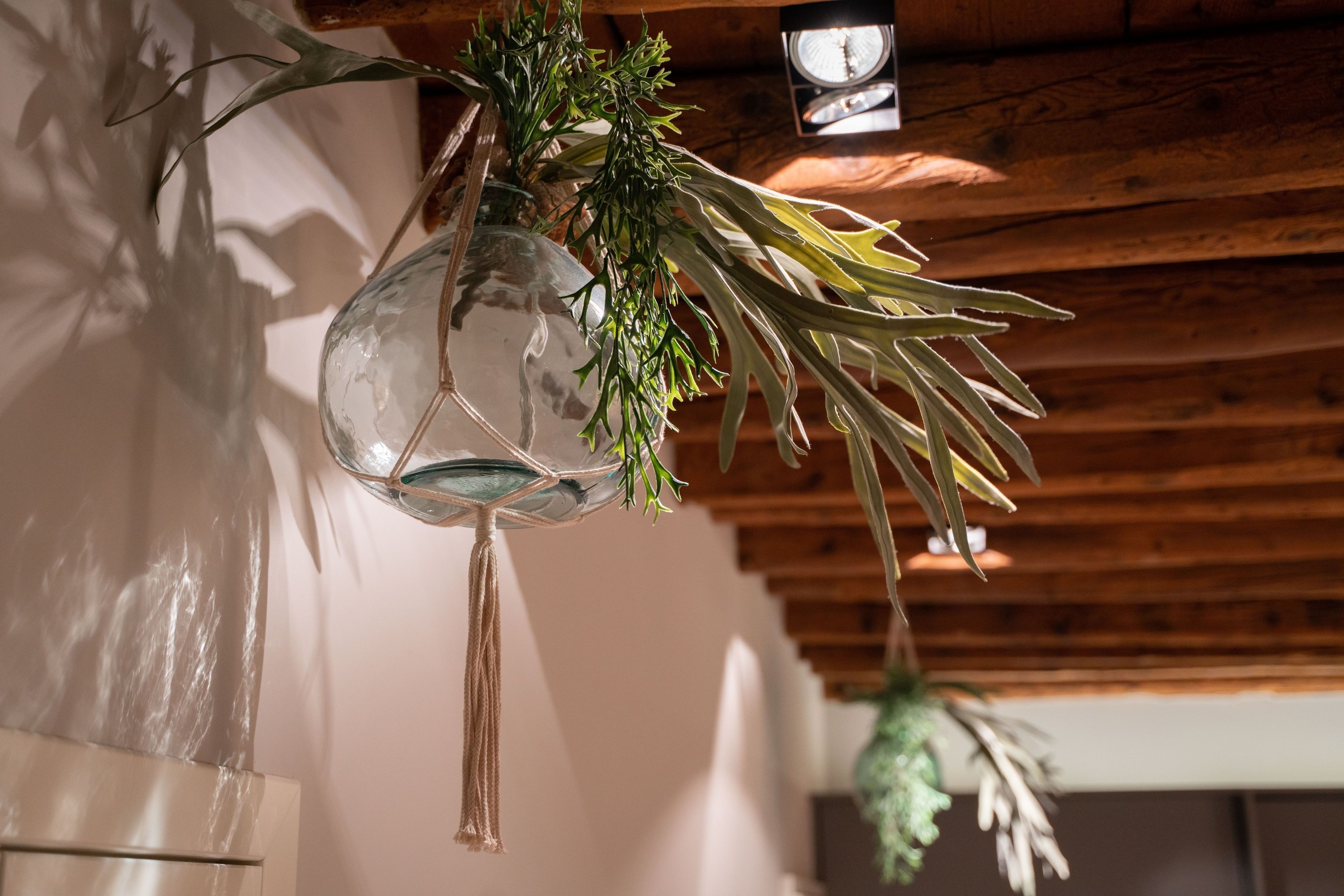 A hanging glass vase with greenery, wooden ceiling beams, and a clock.