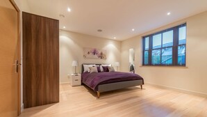 A bedroom with a bed, nightstands, a window, and a painting on the wall. - Hampden Apartments - The Catherine (Windsor)