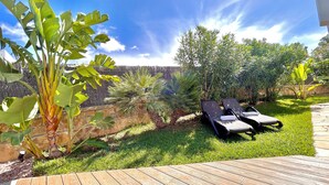 A wooden deck with two lounge chairs, a stone wall, and various tropical plants. - Vacation Villa with Pool and Breathtaking Ocean Views, Last-Minute Deal for September 2026 (Alcudia)