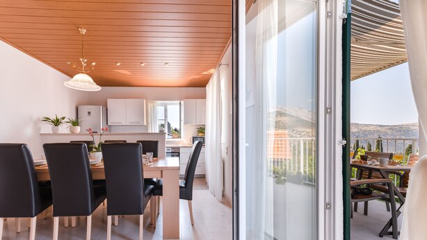 A modern kitchen with white cabinets, a wooden ceiling, and a dining area with black chairs and a wooden table. - Stone house with  pool (Donje Sitno)