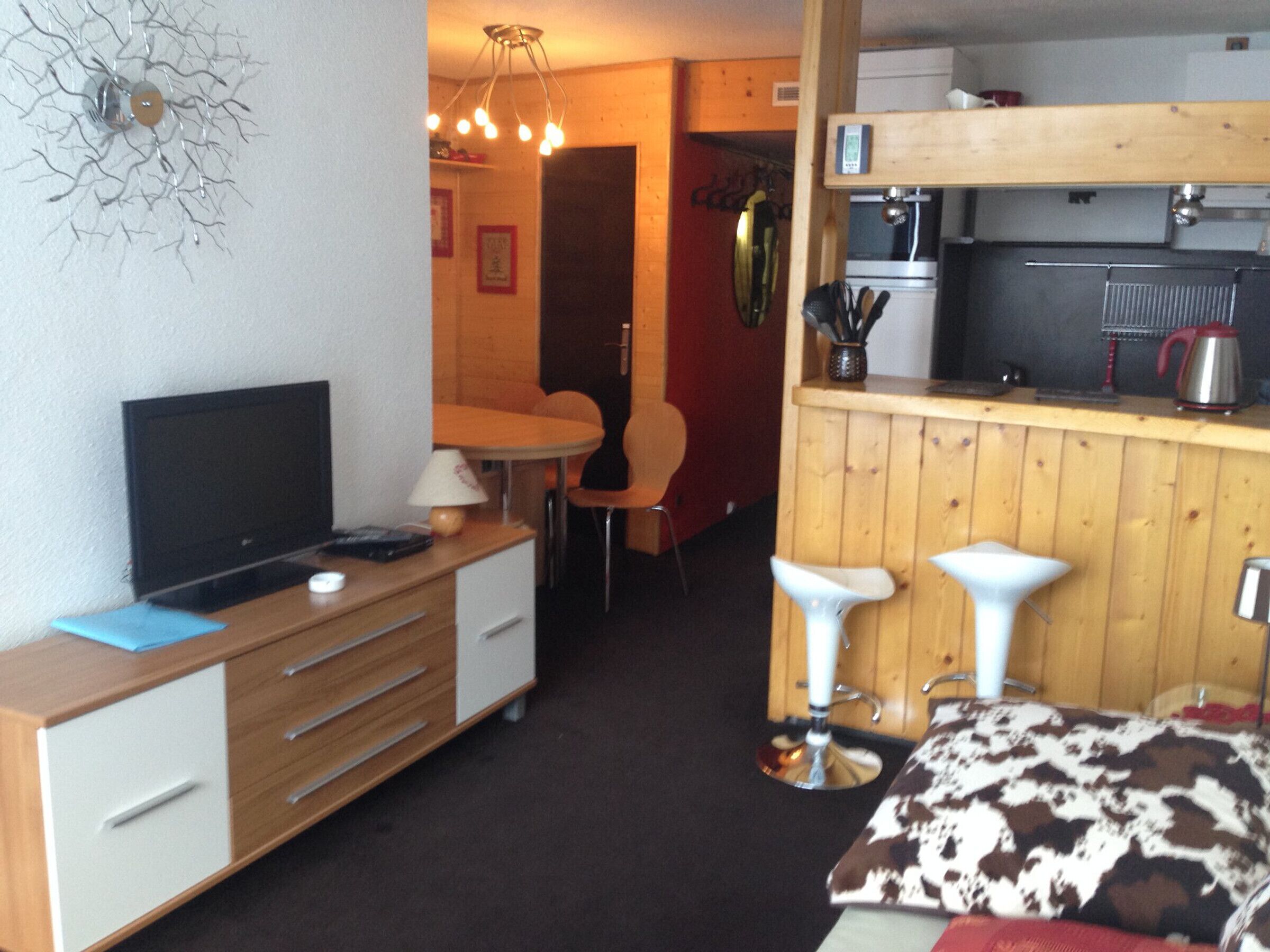 Ett kompakt rum med TV, skrivbord, stol, ett litet matbord och en liten köksdel.
