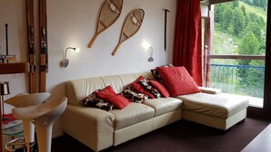A living room with a beige sofa, red cushions, a glass coffee table, and a view of a green landscape through a balcony. - Comfortable 2-room apartment in Arc 2000 for 6 people (Les Arcs 2000)