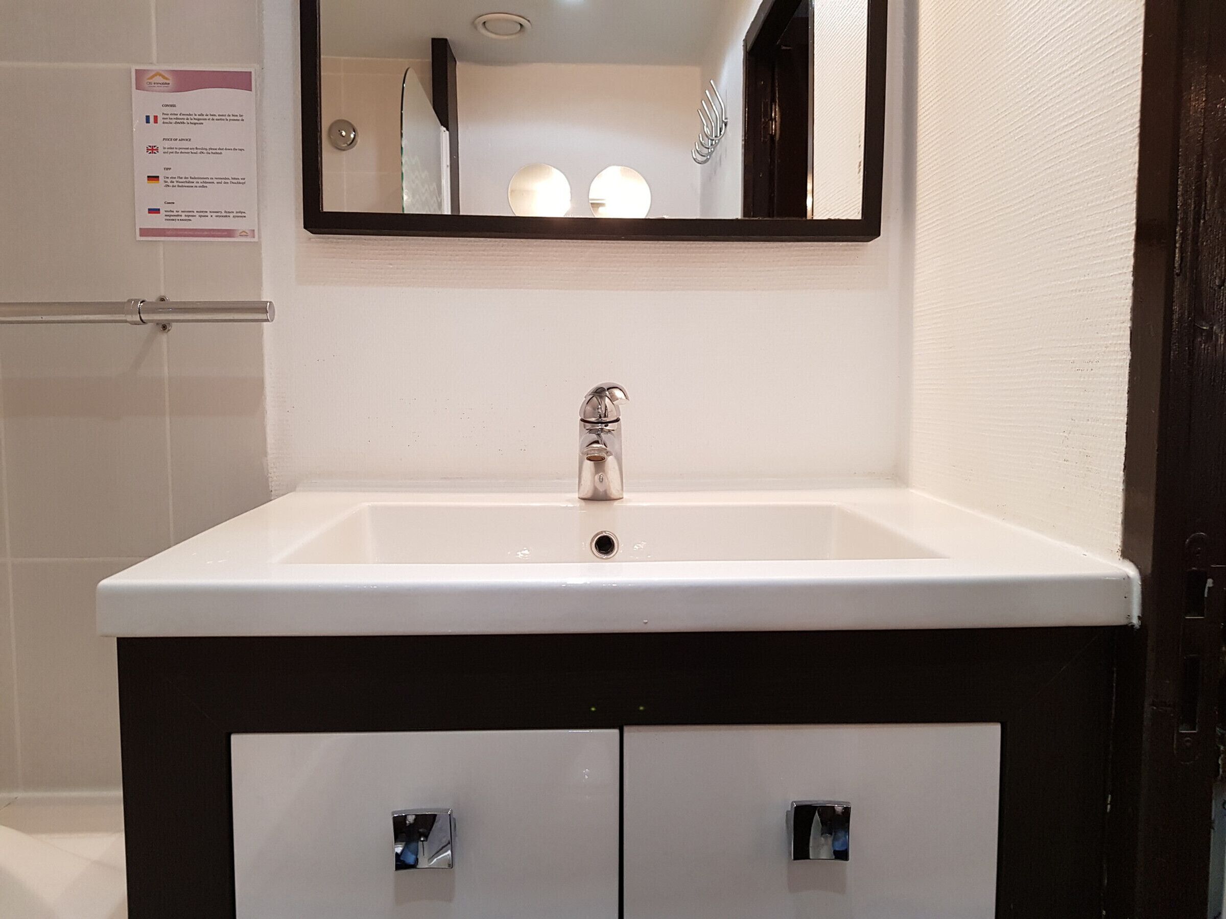 Un baño con un lavamanos blanco, un espejo y un mueble negro con dos cajones.