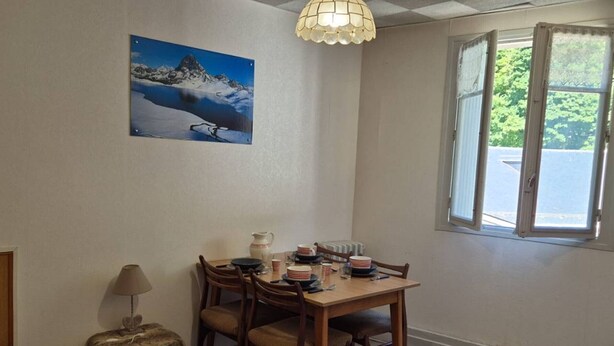 A dining area with a wooden table and chairs, a painting of a mountain landscape, a lamp, and a window with an open door.