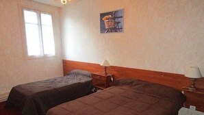 A room with two single beds, a wooden headboard, a small table with a lamp, and a window.