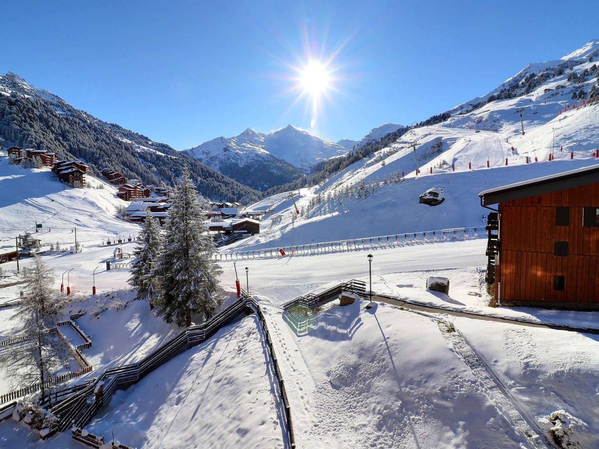 A snow-covered mountain landscape with a wooden building, ski slopes, and a clear sky.