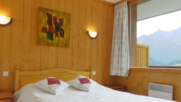 Ein Zimmer aus Holz mit einem Bett, einem Gemälde und einem Fenster mit Blick auf die Berge.