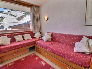 A room with a wooden bed, a red sofa, and a window with a view of a snowy landscape.