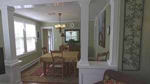 Uma sala de jantar com uma mesa e cadeiras, um candelabro e um sofá vermelho com uma almofada florida.