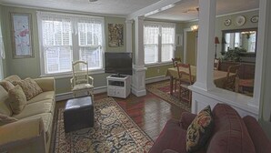 Uma sala de estar com ventilador de teto, televisão, sofá, mesa de centro e um espaço de jantar com mesa e cadeiras.