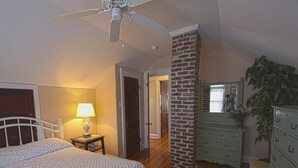 Quarto com cama, mesa de cabeceira, cômoda, abajur, parede de tijolos e ventilador de teto.