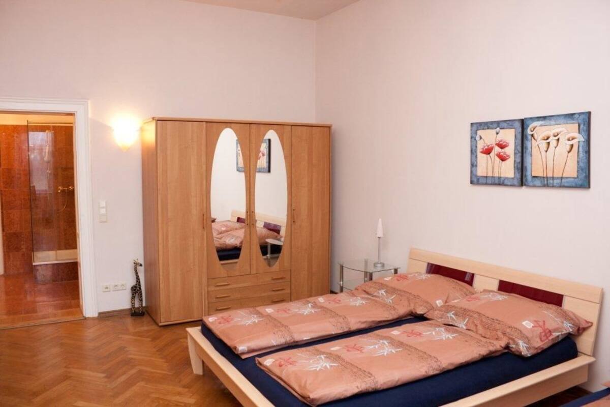 A bedroom with a wooden wardrobe, a bed with floral bedding, and two wall-mounted paintings.