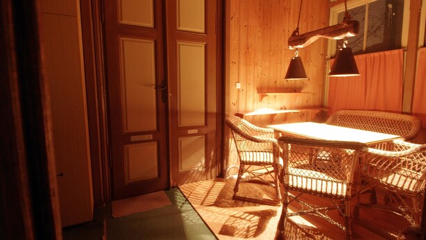 A wooden interior with a dining table and chairs, a hanging light fixture, and a door. - Raisa Apartments (Pressbaum)