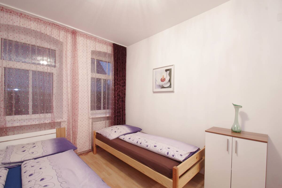 A small bedroom with two single beds, a wooden cabinet, and a window with sheer curtains.