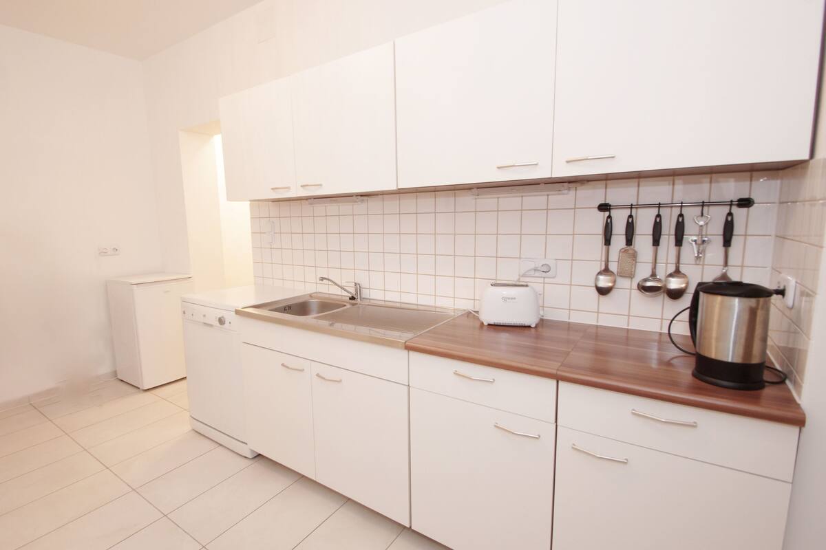 A modern kitchen with white cabinets, a stainless steel sink, a toaster, and a kettle.