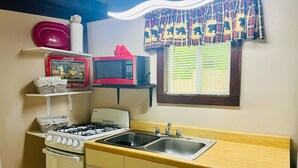 Una cocina compacta con estufa a gas, microondas, pileta y una ventana con persianas.