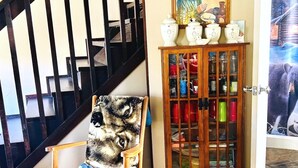 Una mecedora de madera con estampado de lobo, un aparador de madera con puertas de cristal y una escalera con barandillas negras.