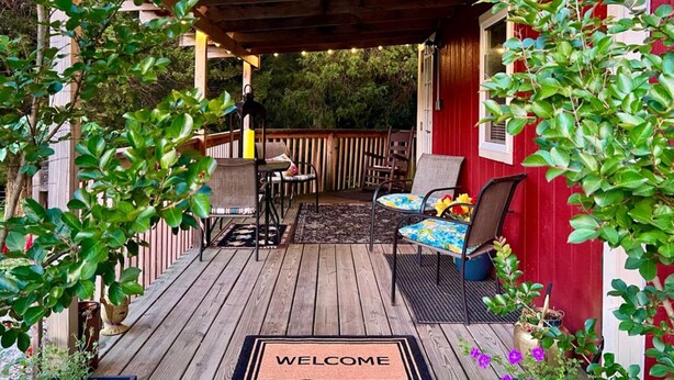 Una terraza de madera con un felpudo, mobiliario exterior y plantas en macetas.
