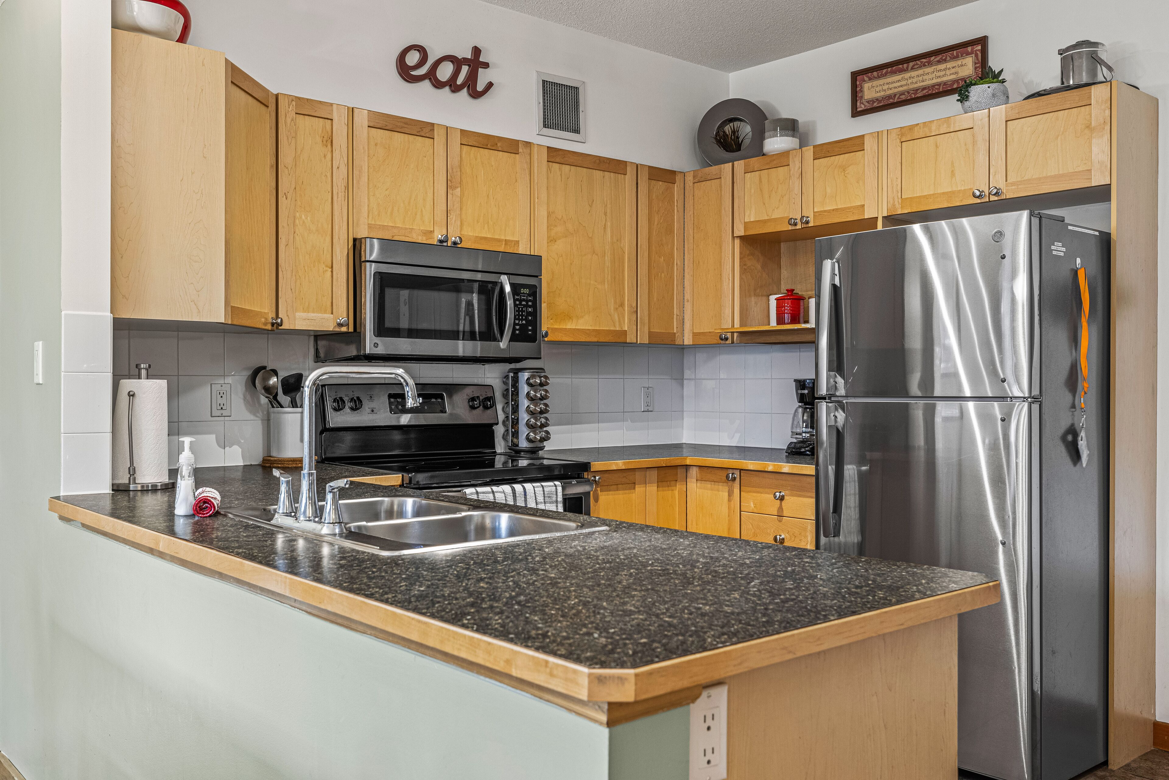 A kitchen with wooden cabinets, a stainless steel refrigerator, a microwave, and a granite countertop.